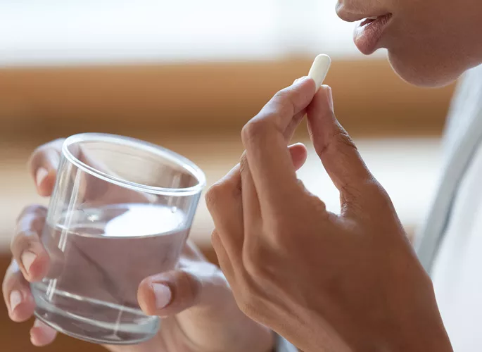 Person holding a glass of water and about to take a pill